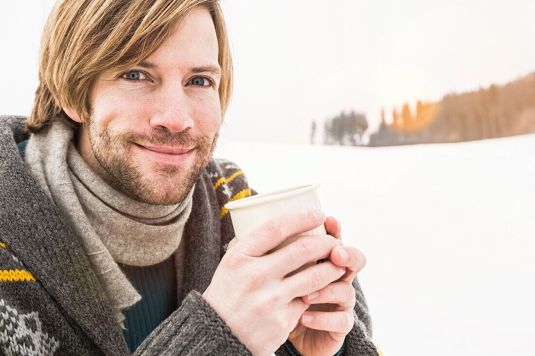 Man wearing knitted cardigan holding hot drink outdoors