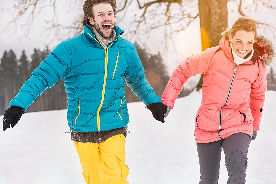 Mid adult couple running in snow holding hands