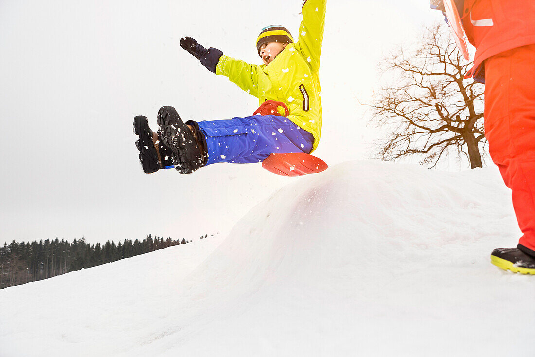 Boy sledging over bump in snow