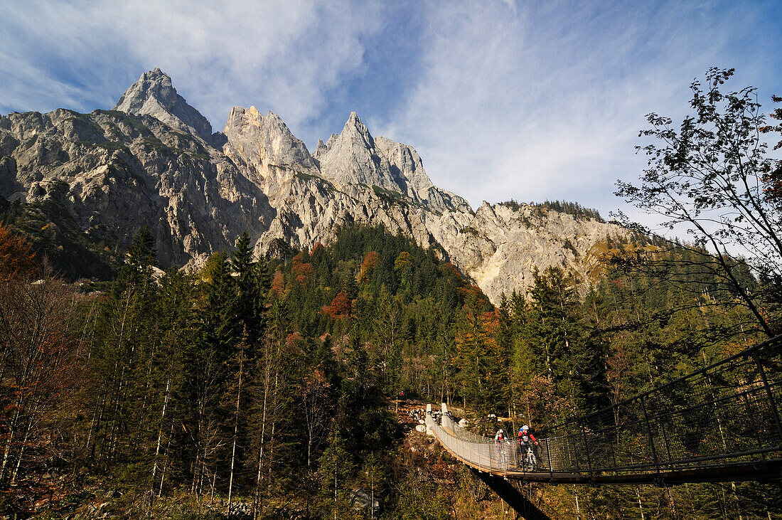 Mountain bikers passing chain bridge crossing Klausbach valley, Muehlsturzhoerner in background, Ramsua, Berchtesgadener Land, Upper Bavaria, Germany