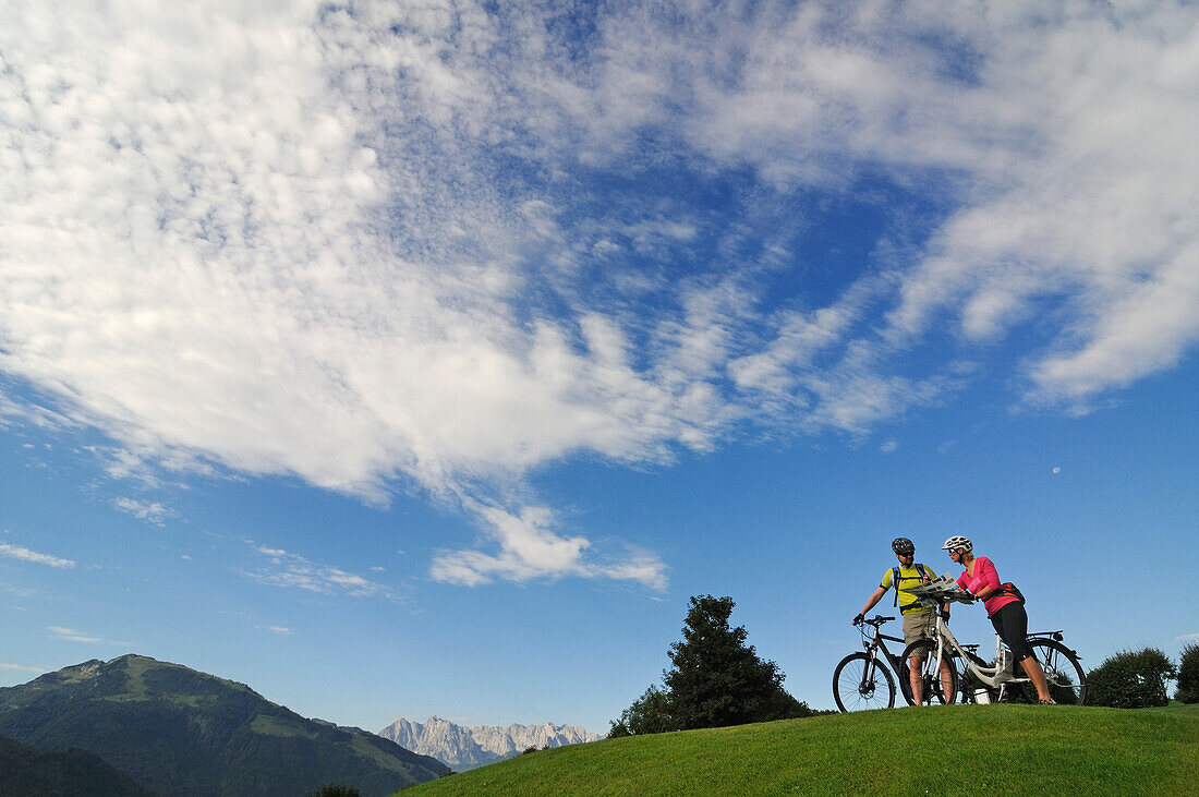 Couple with e-bikes, Wilder Kaiser mountains in background, Reit im Winkl, Chiemgau, Upper Bavaria, Germany