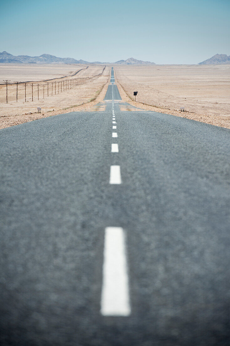 asphaltierte Straße und Strommasten bis zum Horizont in der Wüste vor Lüderitz, Namibia, Afrika