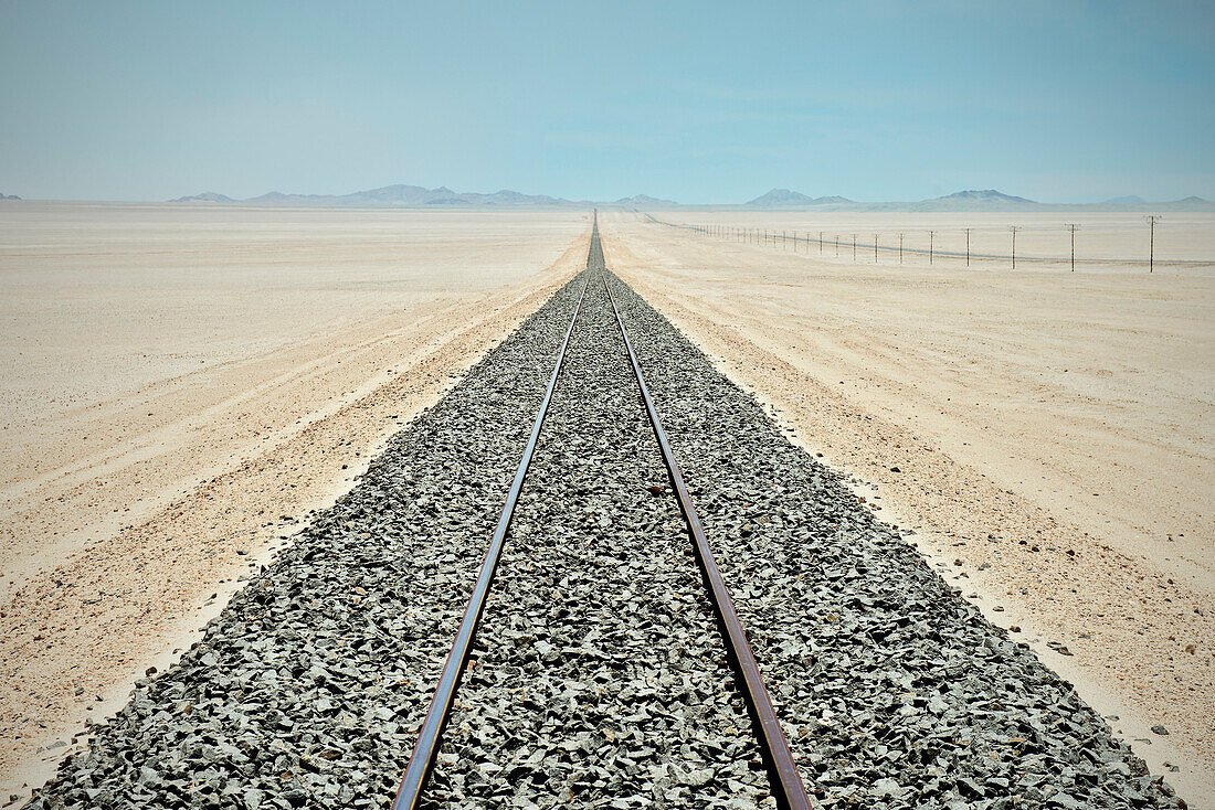 Gleise und Strommasten bis zum Horizont in der Wüste vor Lüderitz, Namibia, Afrika