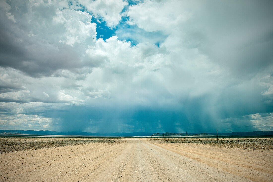 staubige Straße mit starkem Regen und Gewitter am Horizont, Tiras Gebirge, Tirasberge, Namib Naukluft Park, Namibia, Afrika