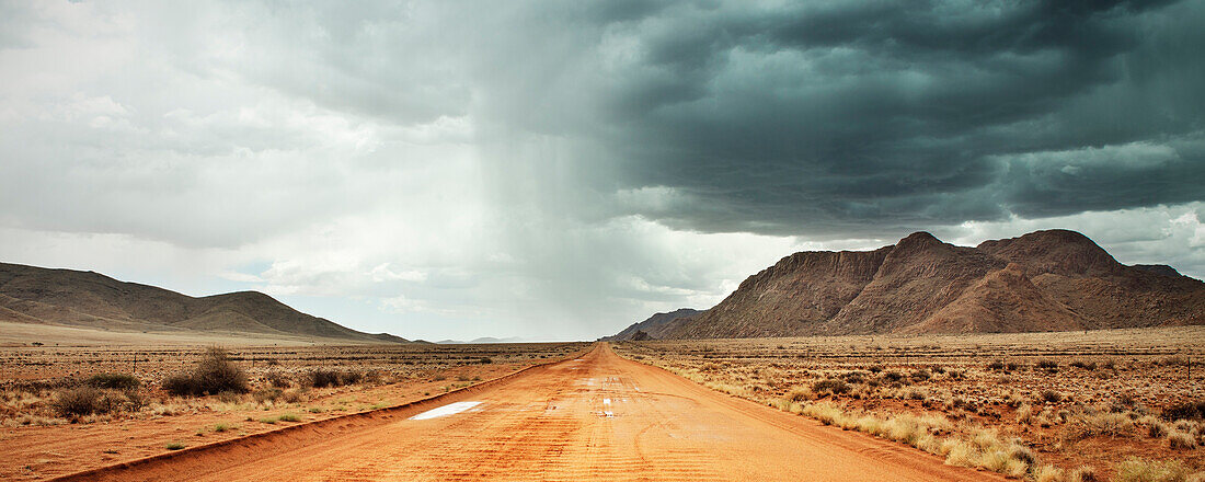Red sandy road with heavy rainfall and thunderstorm in the distance, Tiras Mountain Range, Namib Naukluft National Park, Namibia, Africa