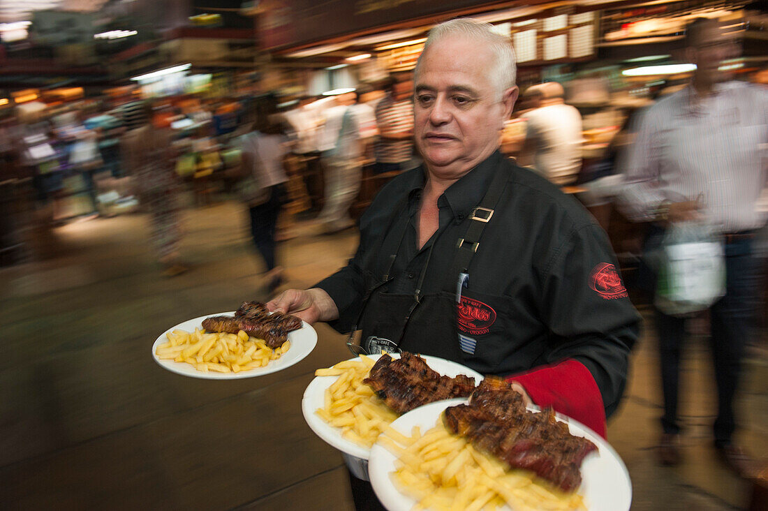 Kellner serviert Teller mit Steak und Pommes Frites in einem Parilla Restaurant im Mercado del Puerto, Montevideo, Montevideo, Uruguay