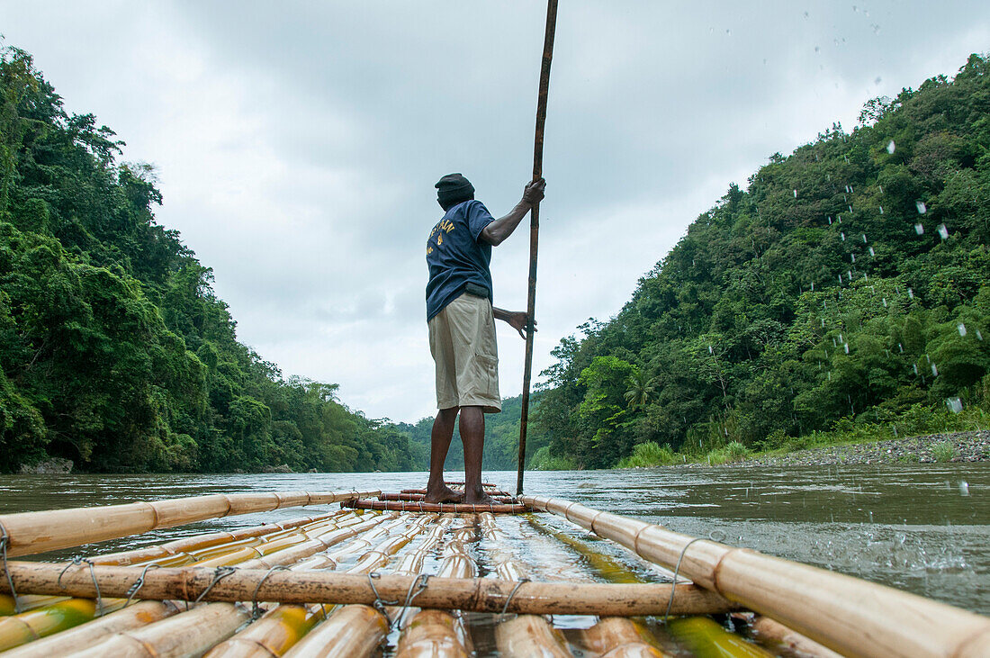 Mann steuert ein traditionelles Floß aus Bambus auf dem Fluss Rio Grande, Port Antonio, Portland, Jamaika
