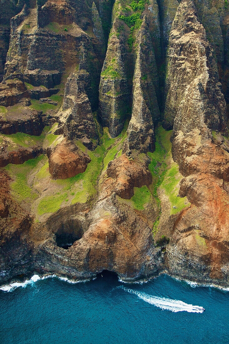 'Aerial view of the rugged coastline and a boat in the pacific ocean along an hawaiian island; Hawaii, United States of America'