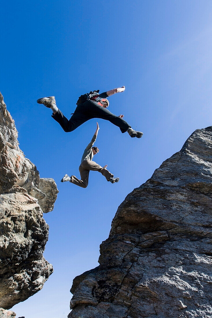 Hikers Leap Between Rocks Near Noatak River In The Brooks Range, Gates Of The Arctic National Park, Northwestern Alaska, Above The Arctic Circle, Arctic Alaska, Summer.