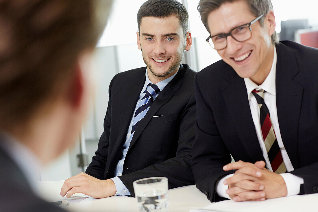 Businessmen sitting around conference table having meeting, smiling