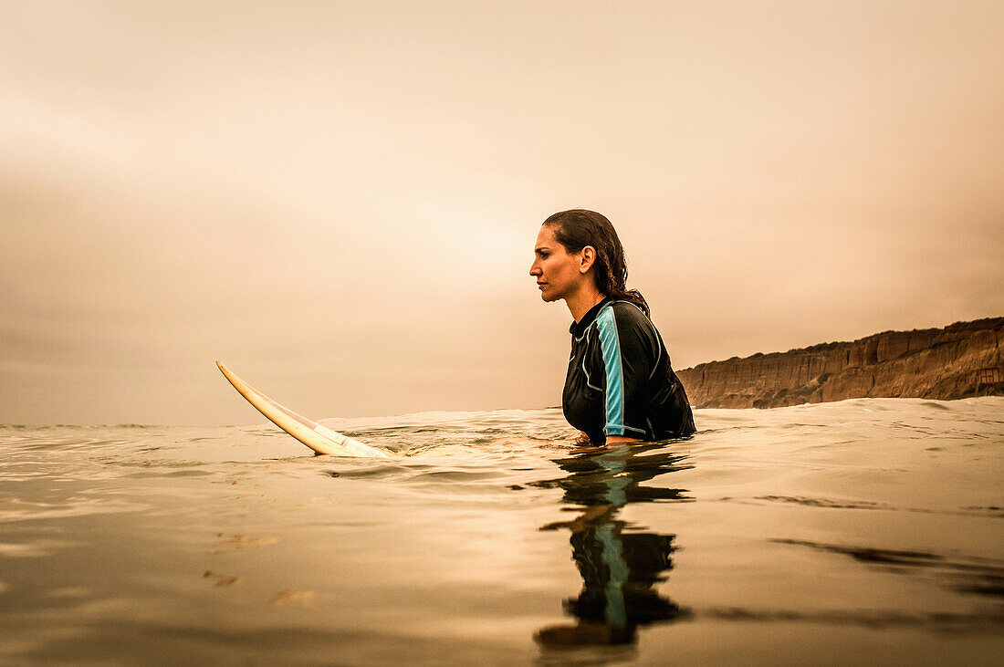Young woman in sea with surfboard, profile