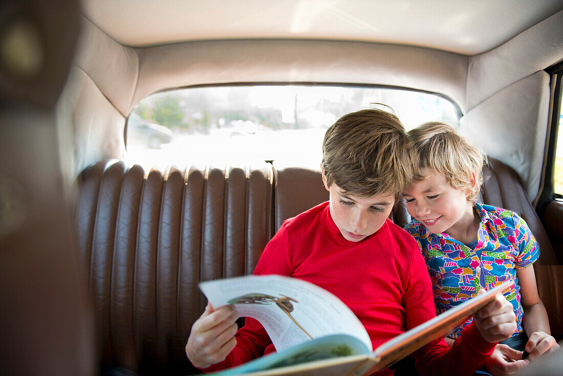 Boys sitting in back of car reading book