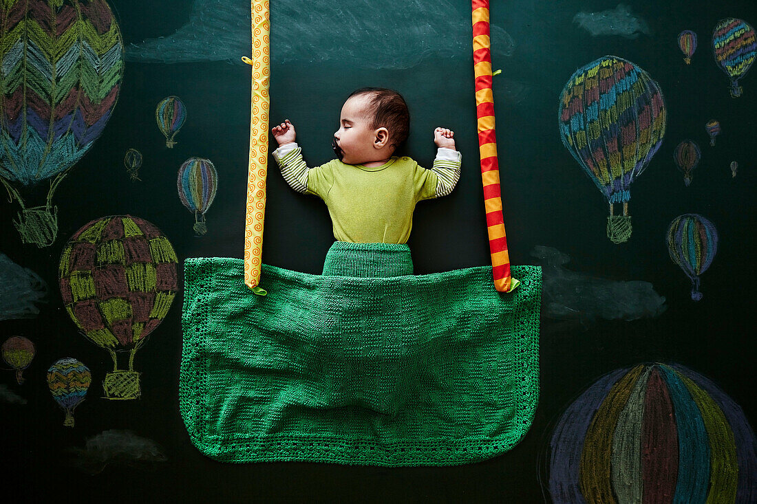 Baby girl sleeping against drawings on blackboard, overhead view