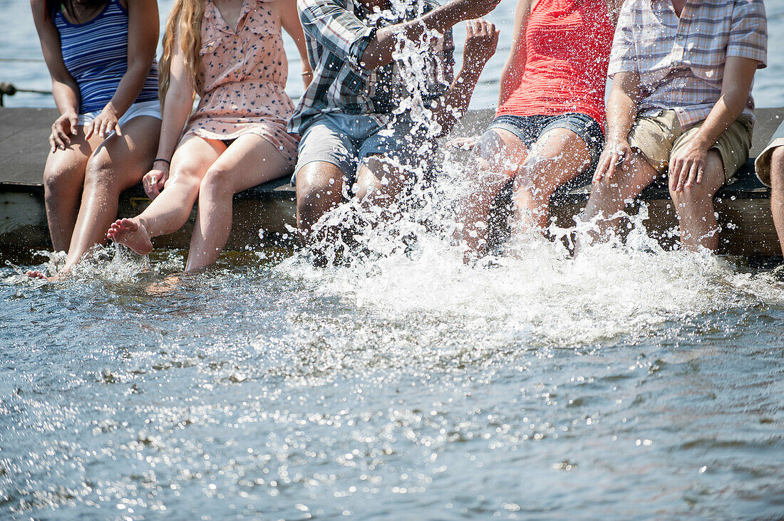 Friends sitting on jetty splashing in lake