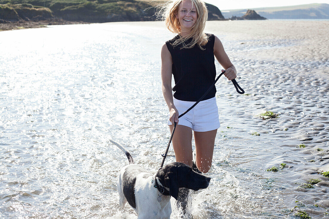Woman walking dog on beach, Wales, UK