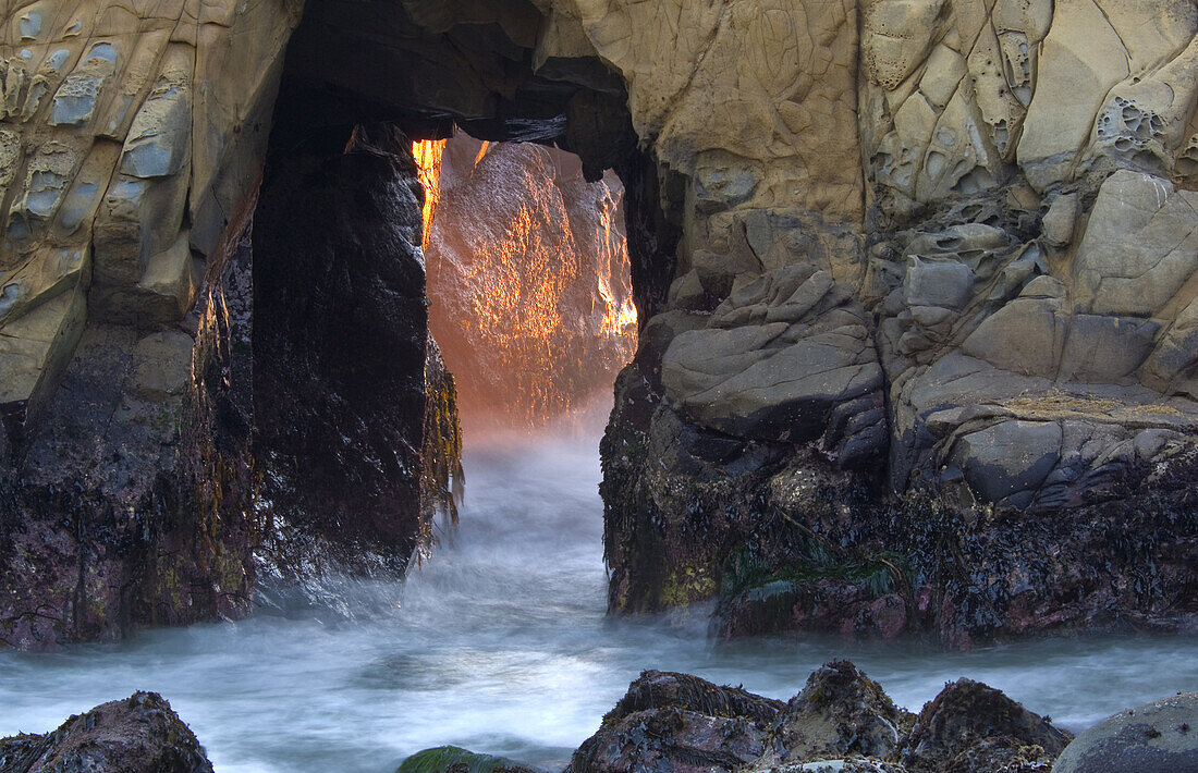 Sunset light and waves coming through hole in coastal rock at Pfeiffer Beach, Big Sur, California.
