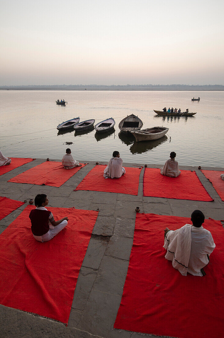 Five children on red carpet waits for sunrise doing yoga on the banks of the Ganges river in Varanasi, India