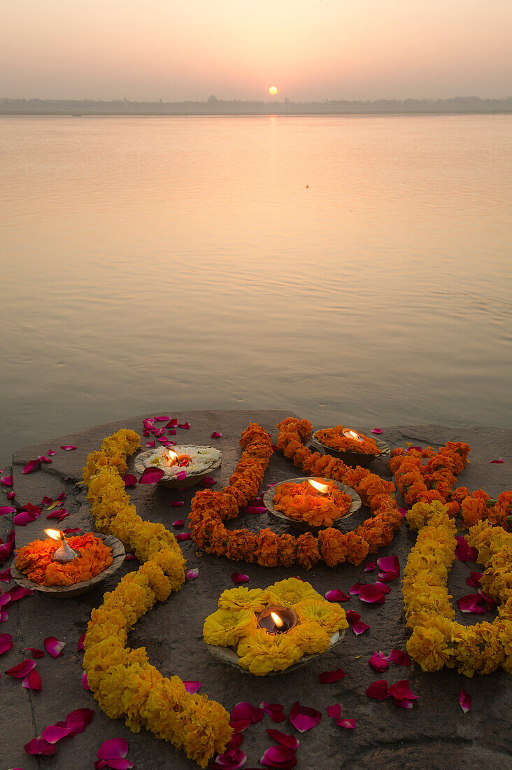 Lights and garlands of flowers on the banks of Ganges river at sunrise with rising sun in the background, Varanasi, India