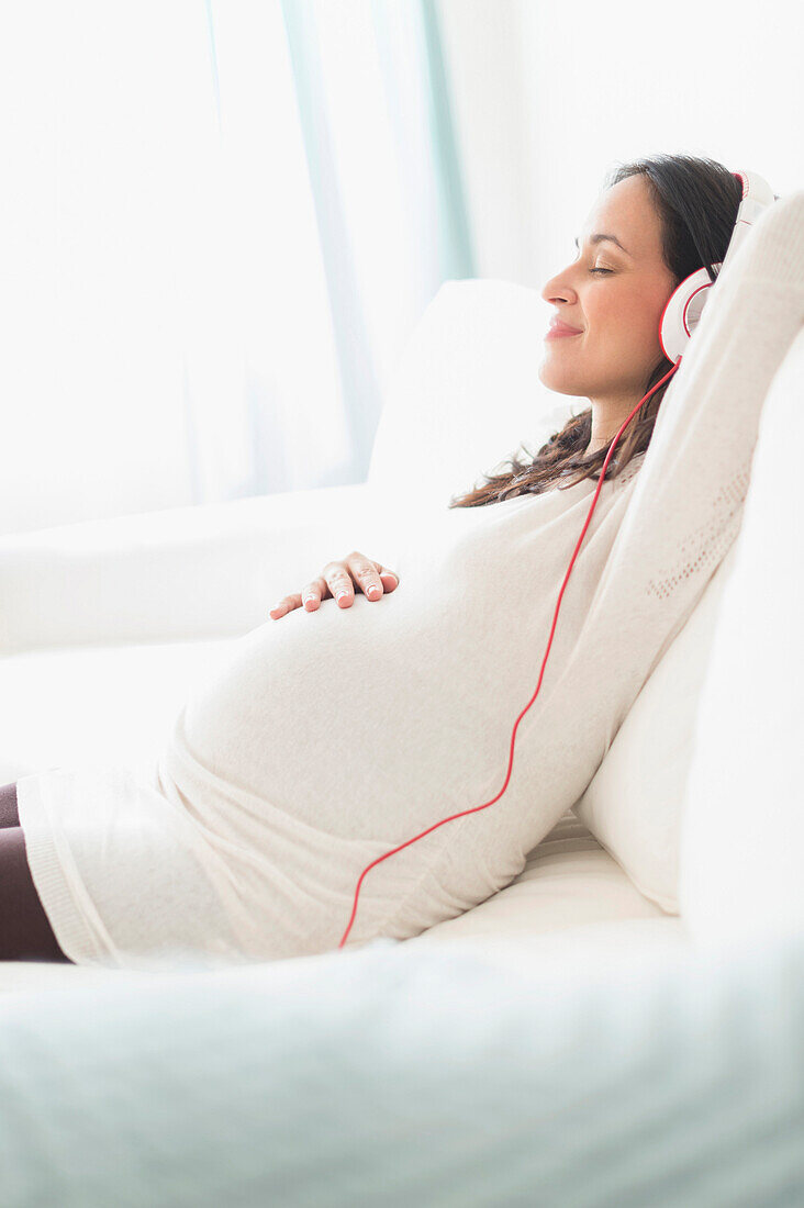 Pregnant Hispanic woman listening to headphones, Jersey City, NJ, USA