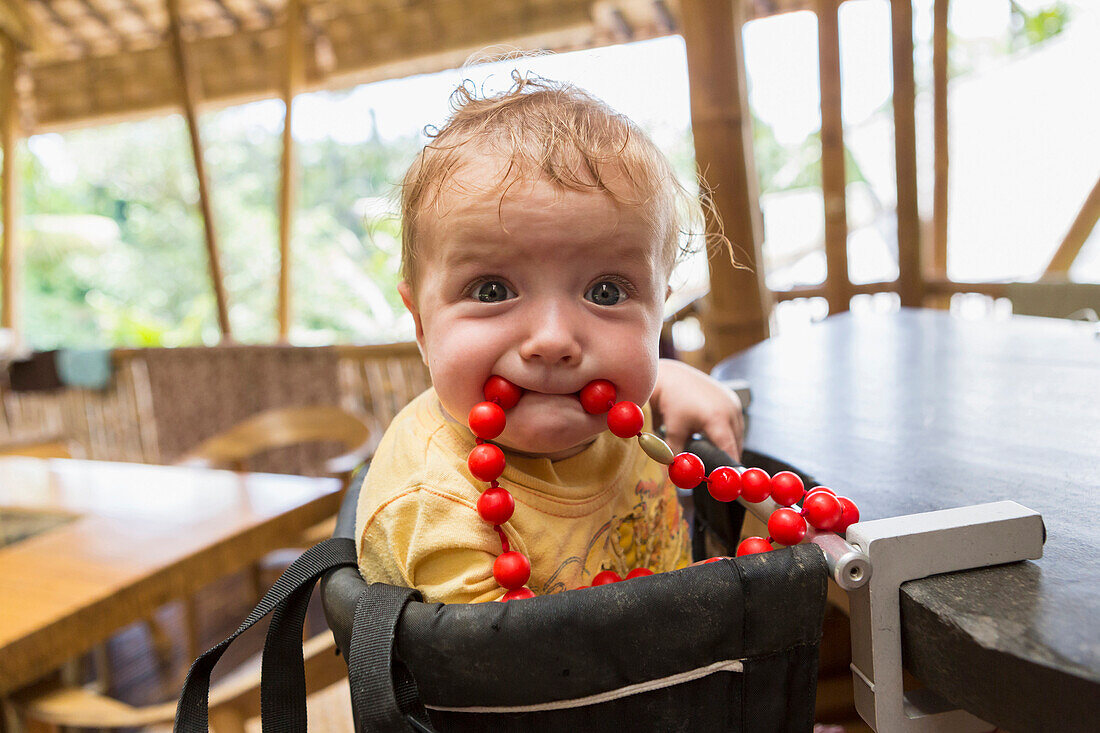 Caucasian baby playing with beads in high chair, Ubud, Bali, Indonesia