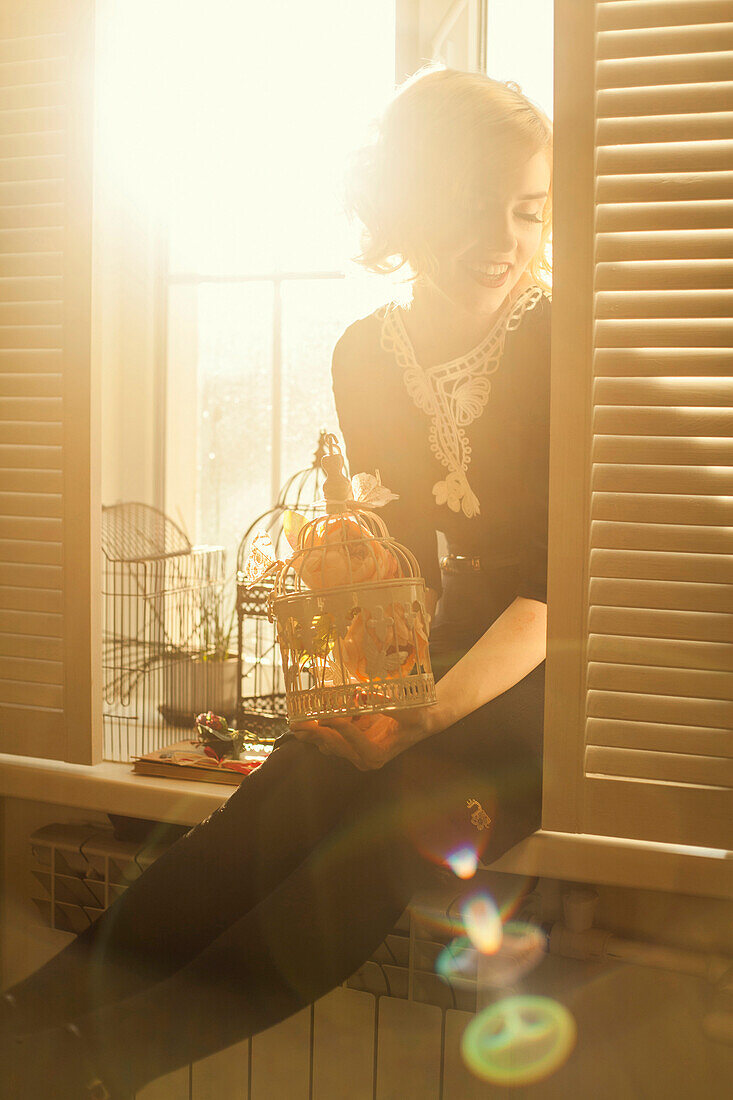 Caucasian woman holding birdcage in window, Nizhniy Tagil, Sverdlovsk region, Russia