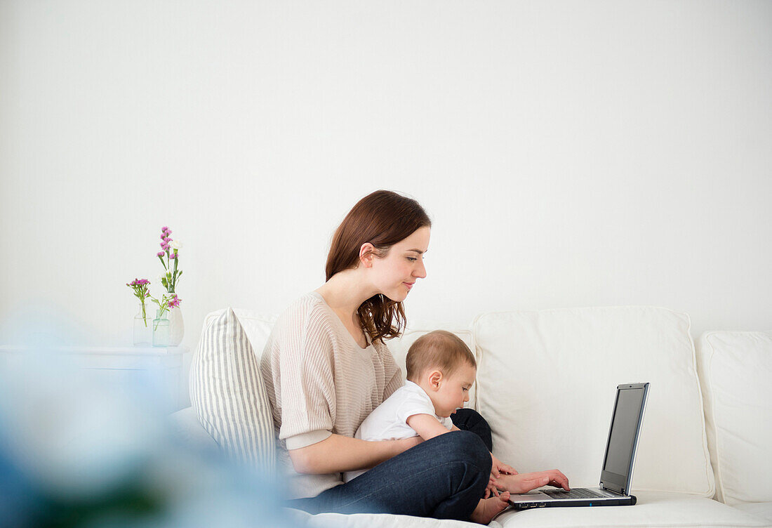 Mother and baby using laptop on sofa, Jersey City, New Jersey, USA