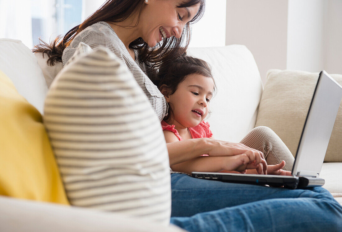 Hispanic mother and daughter using laptop on sofa, Jersey City, New Jersey, USA