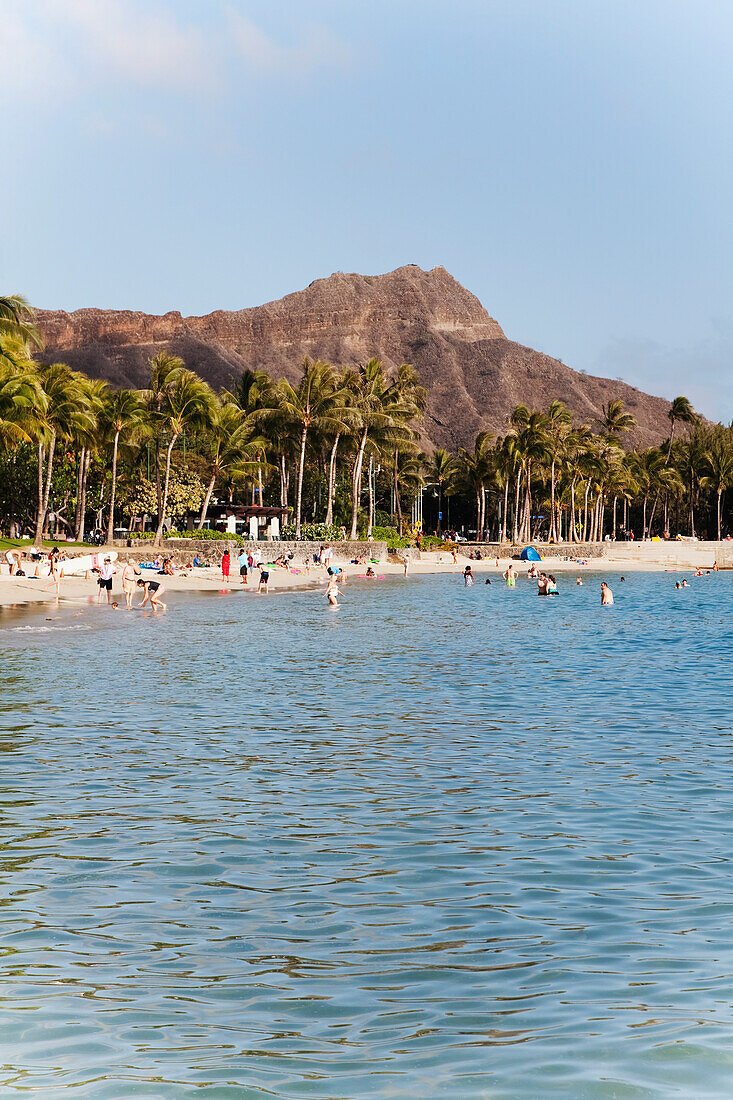 'Mountain, palm trees and beach wit people swimming in the ocean along the coast; Honolulu, Oahu, Hawaii, United States of America'