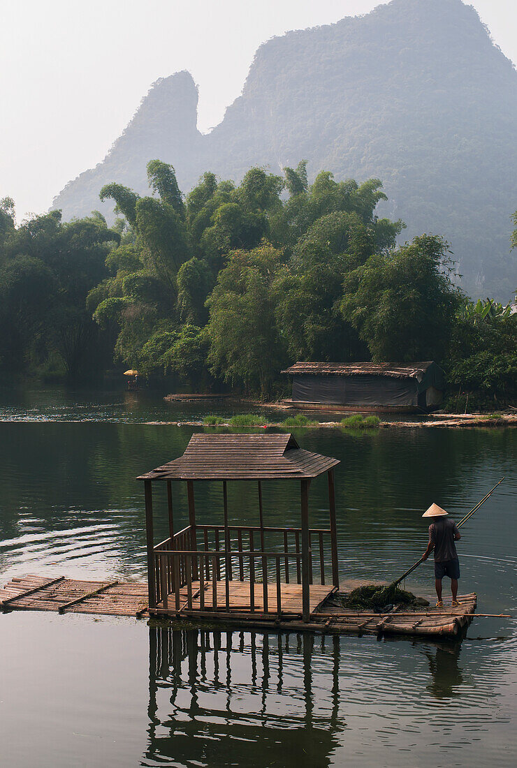 'A Man Paddles Down A River With Mountain Peaks In The Background; Yangshuo, China'