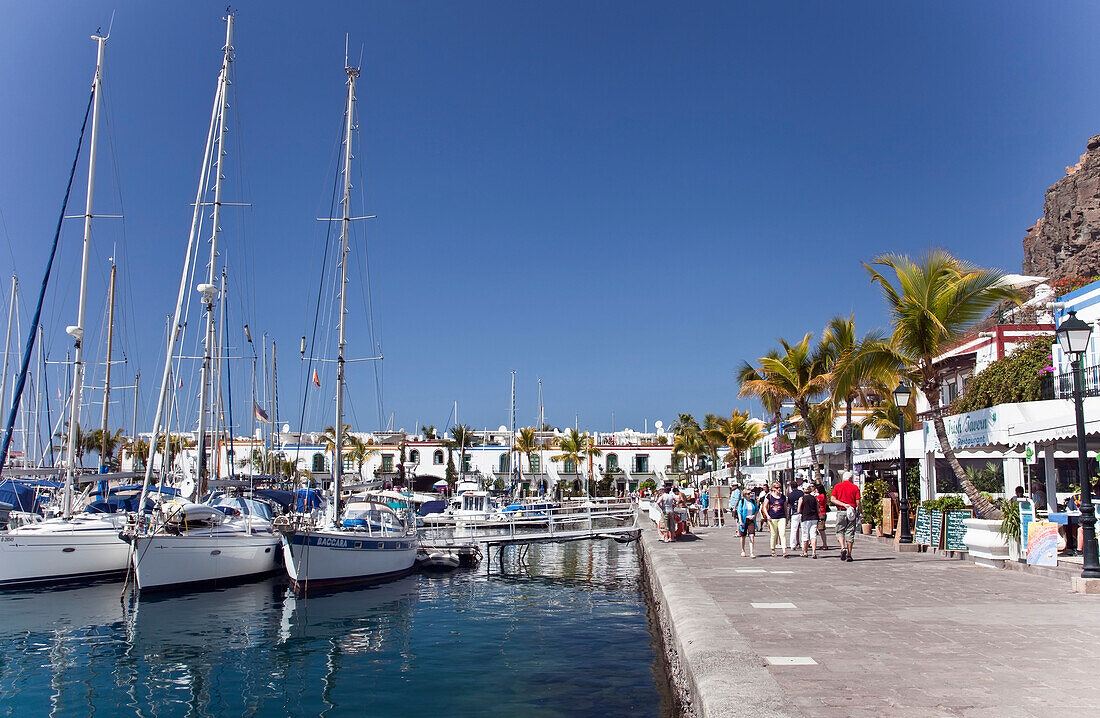'Boats In The Harbour And Pedestrians On The Promenade; Puerto Morgan, Gran Canaria, Spain'