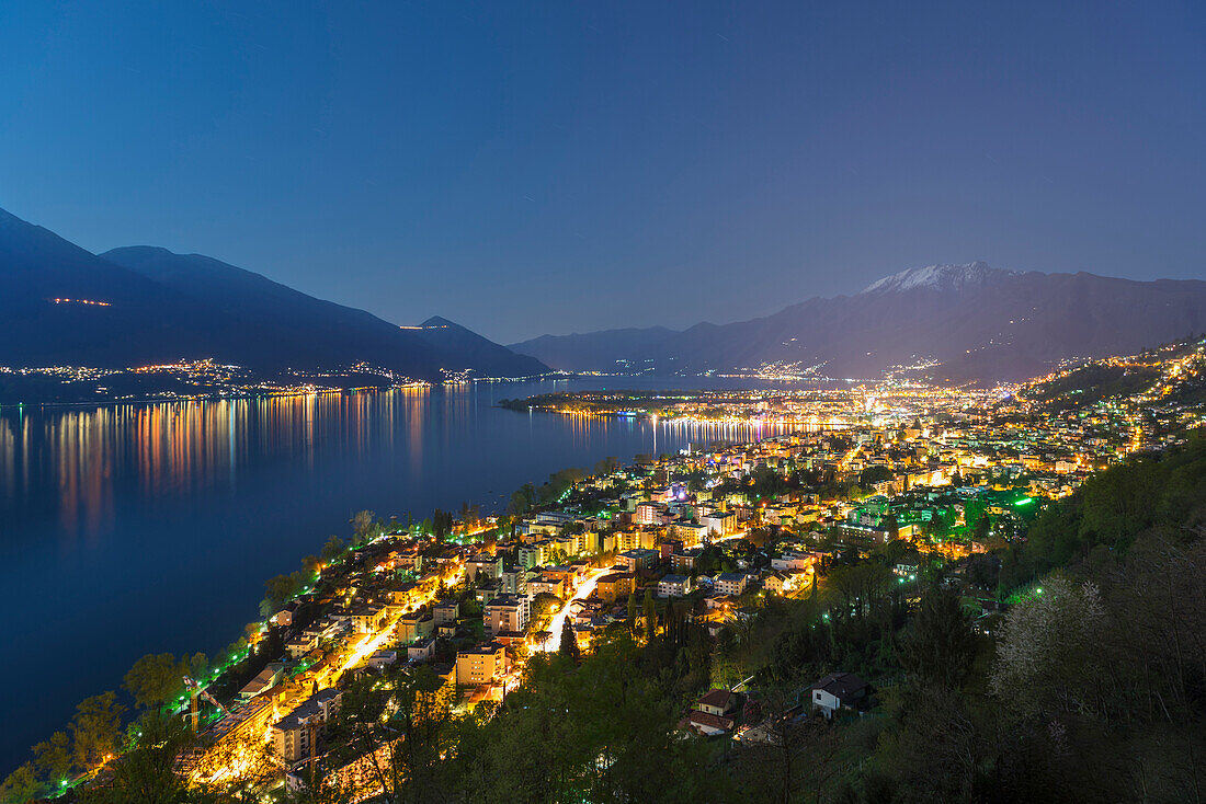 'Buildings Along Lake Maggiore And The Swiss Alps Illuminated By Moonlight At Night; Locarno, Ticino, Switzerland'