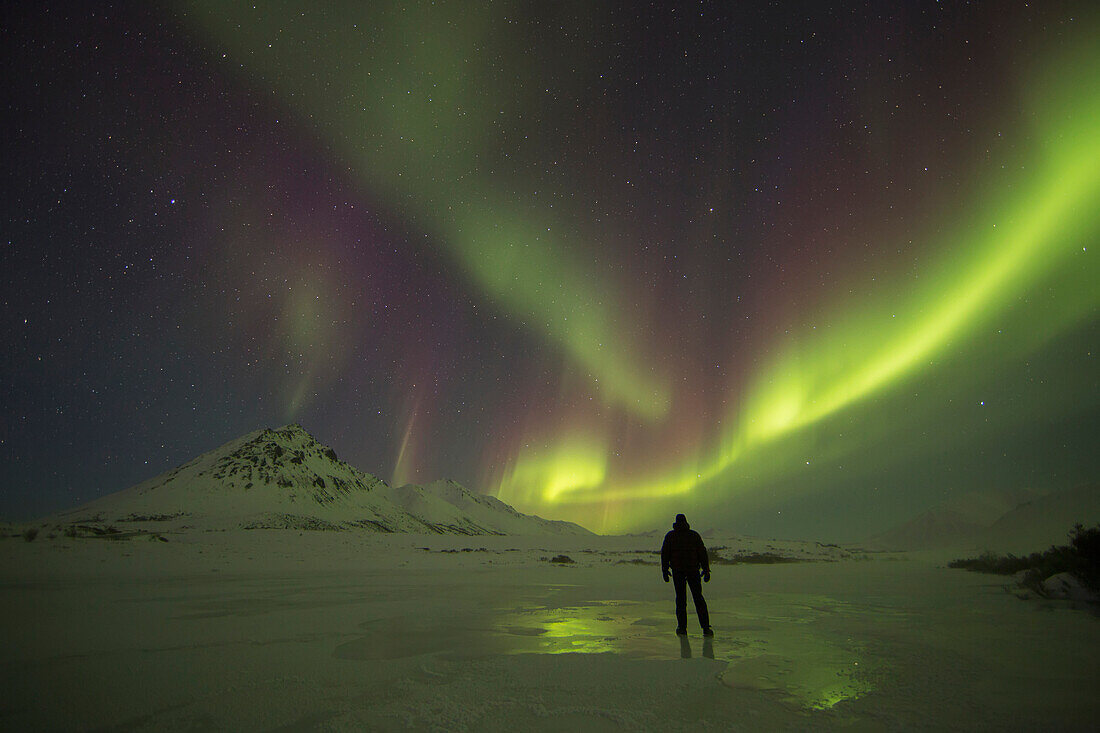 'A Person Stands On The Frozen Blackstone River Beneath The Northern Lights; Yukon, Canada'