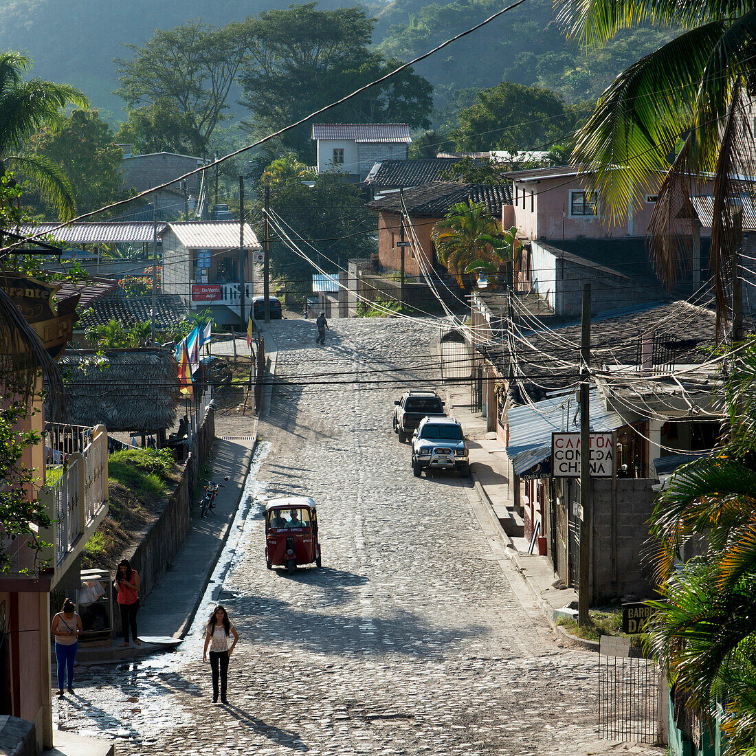 'A Street With Pedestrians, Cars, Buildings And Lush Vegetation; Copan, Honduras'