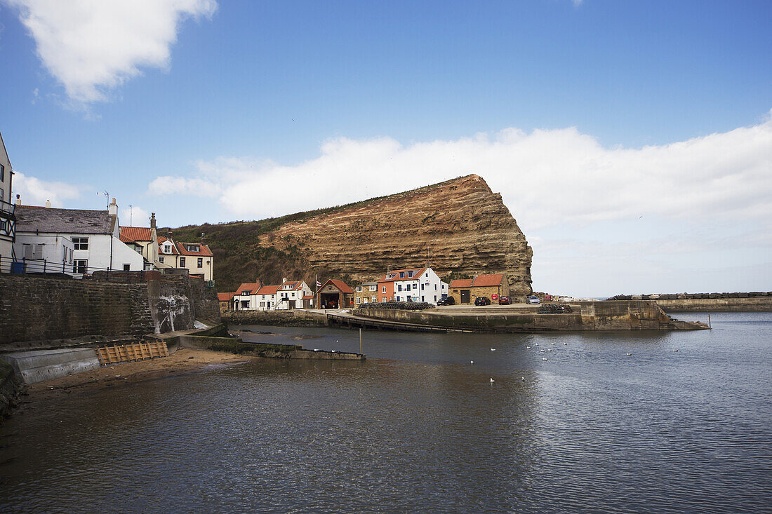 'Houses Along The Water's Edge And A Rock Cliff; Staithes, Yorkshire, England'