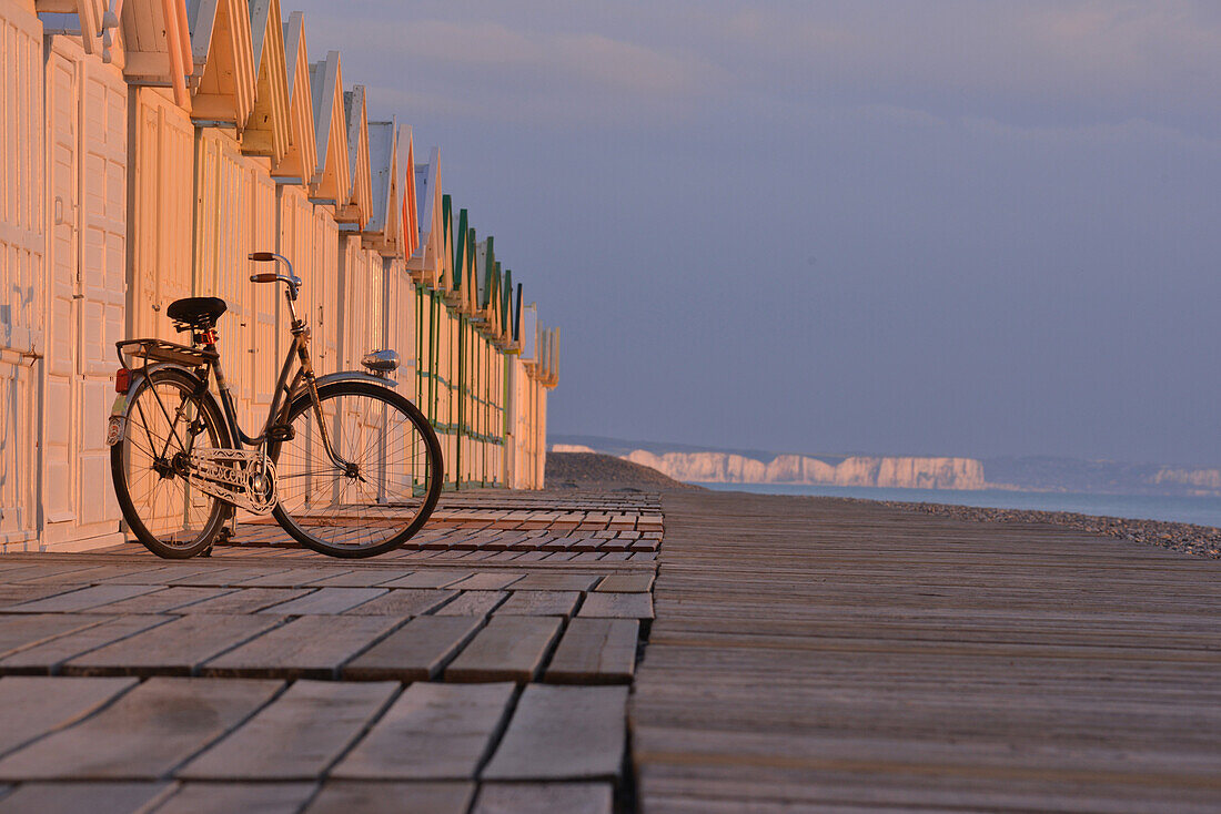 Beach huts and bicycle in cayeux-sur-mer with the cliffs of ault in the background, somme, picardy, france