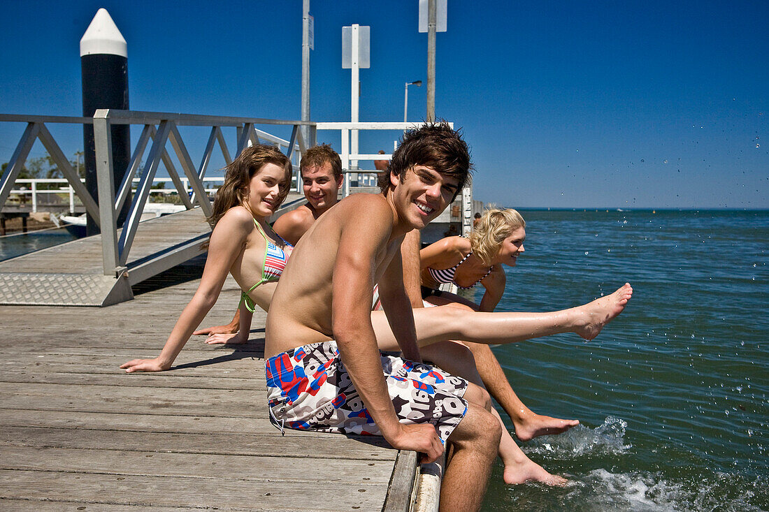 Two Smiling Young Couples Sitting on Edge of Pier