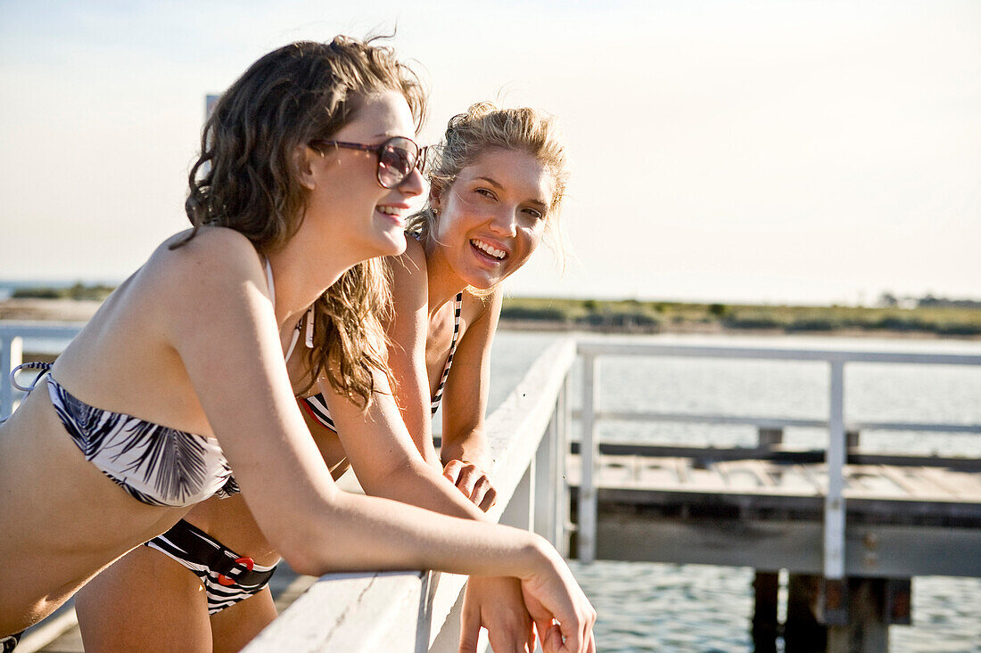 Two Young Women Leaning on Railing on Side of Pier
