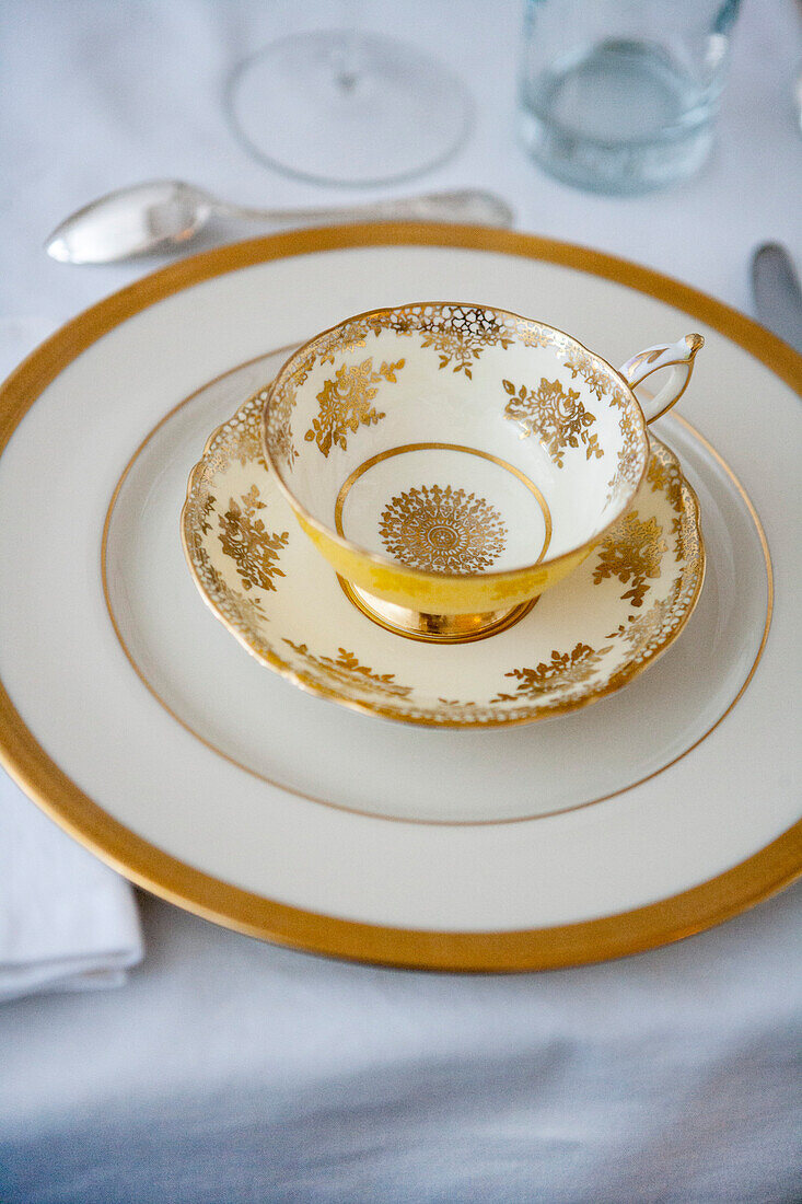 Formal Dining Table Setting with Gold-Accented Teacup and Saucer on Plate with Silverware
