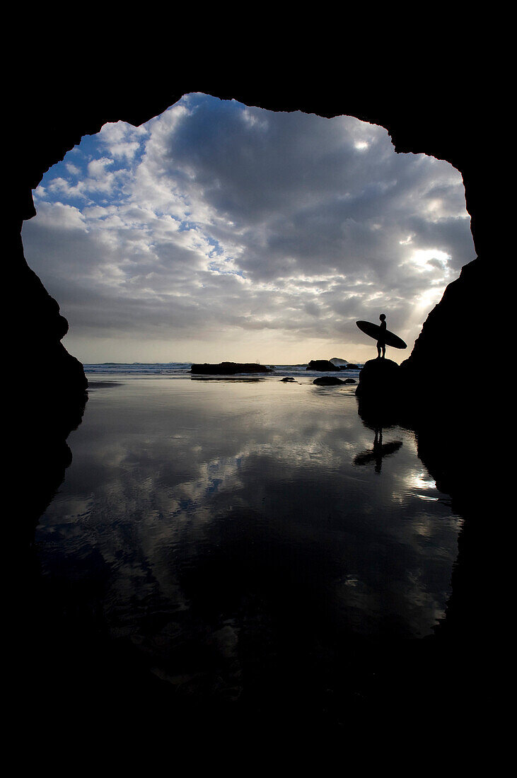 Silhouette Of Surfer On Beach Through Cave, Muriwai Beach, North Island, New Zealand