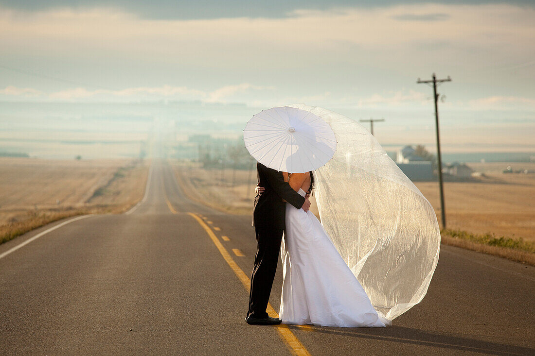 'Bride And Groom In An Embrace Standing On A Road In Rural Alberta; Three Hills, Alberta, Canada'