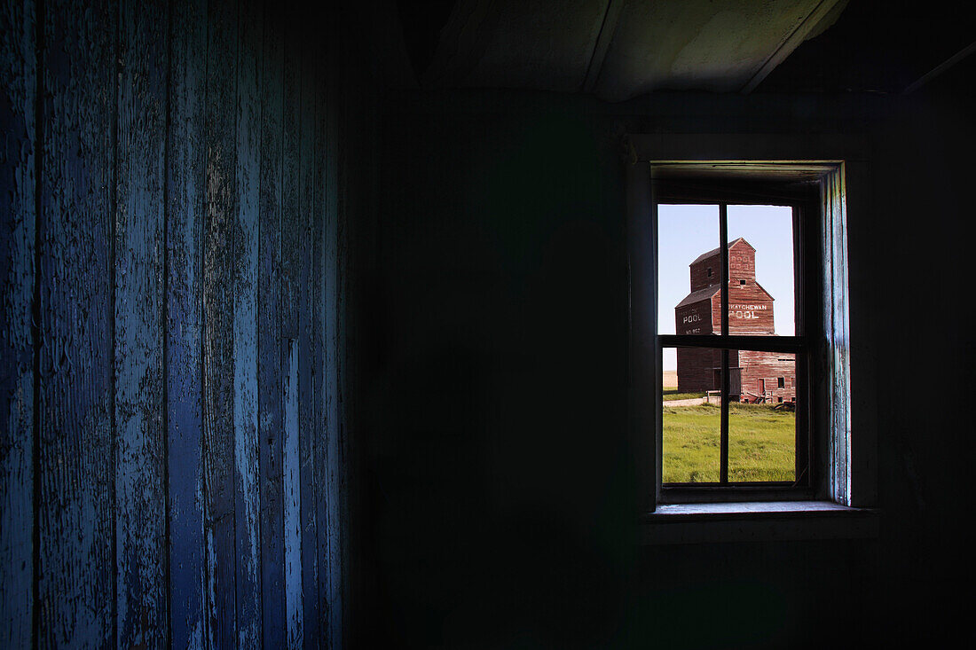 'A Grain Elevator Seen Through The Window Of An Old, Abandoned Ghost Town Store; Bents, Saskatchewan, Canada'