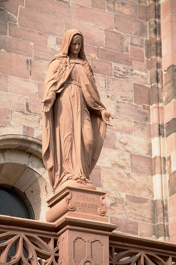 'Sandstone Statue Of Mary Looking Down On Top Of A Rail With Stone Work Of A Cathedral In The Background; Freiburg, Germany'