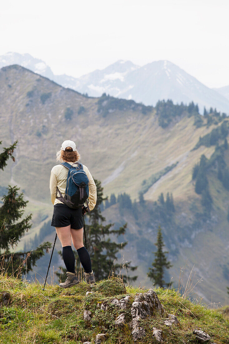 'Female Hiker On A Grassy Viewpoint Overlooking A Mountain Valley And Range; Oberstdorf, Germany'