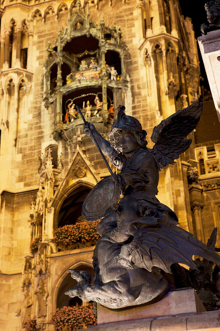 'Winged Statue With A Lit City Hall Tower And Glockenspiel In The Background At Night; Munich, Germany'