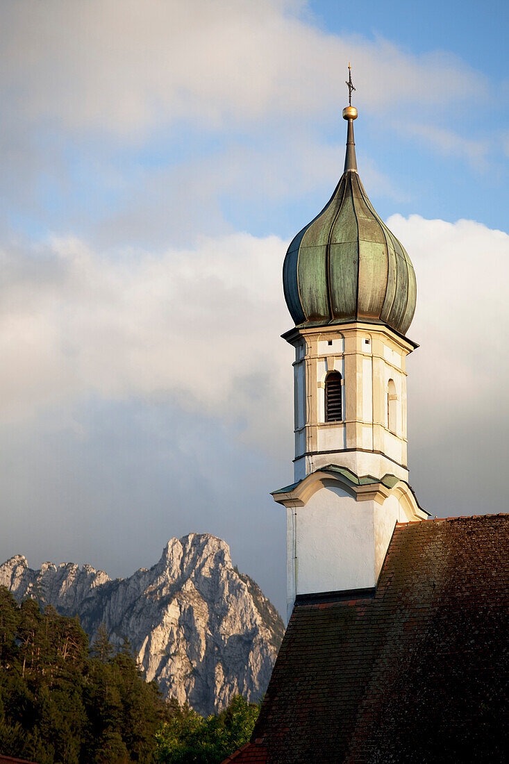 'Church Bell Tower With A Mountain Peak In The Background; Fussen, Germany'