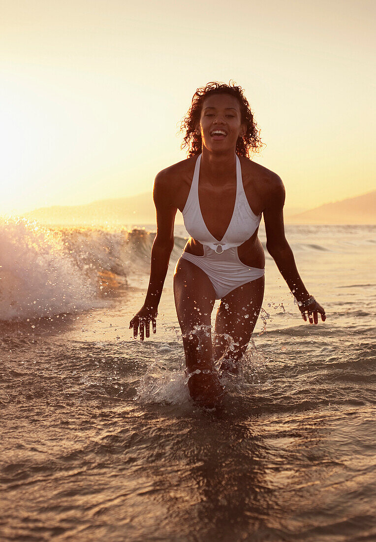 'A Woman In A Bathing Suit Splashes In The Ocean At Sunset Off Los Lances Beach; Tarifa, Cadiz, Andalusia, Spain'