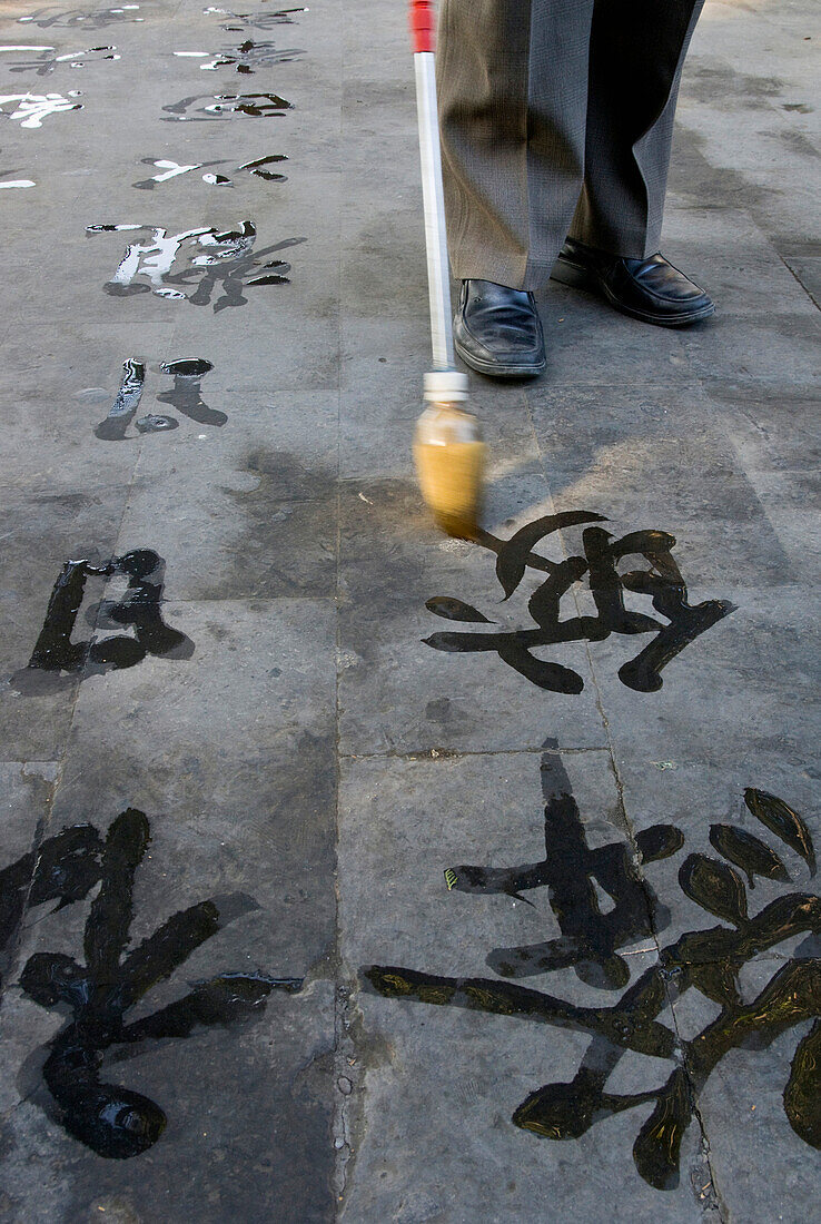 China. Beijing. The Summer Palace. Man Writing Chineese Characters On The Floor With Large Water Brush. Close Up On Characters With Brush And Feet © Eitan Simanor / Axiom