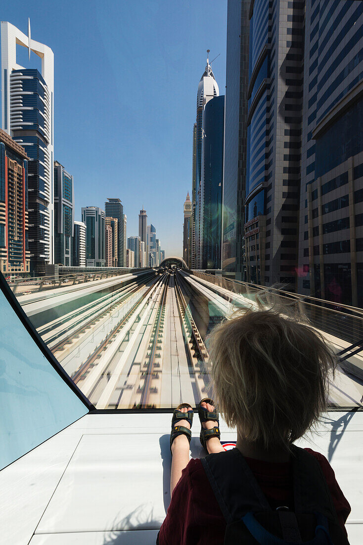'Young boy sitting at the front of metro train as it travels through the business district of Dubai; Dubai, United Arab Emirates'