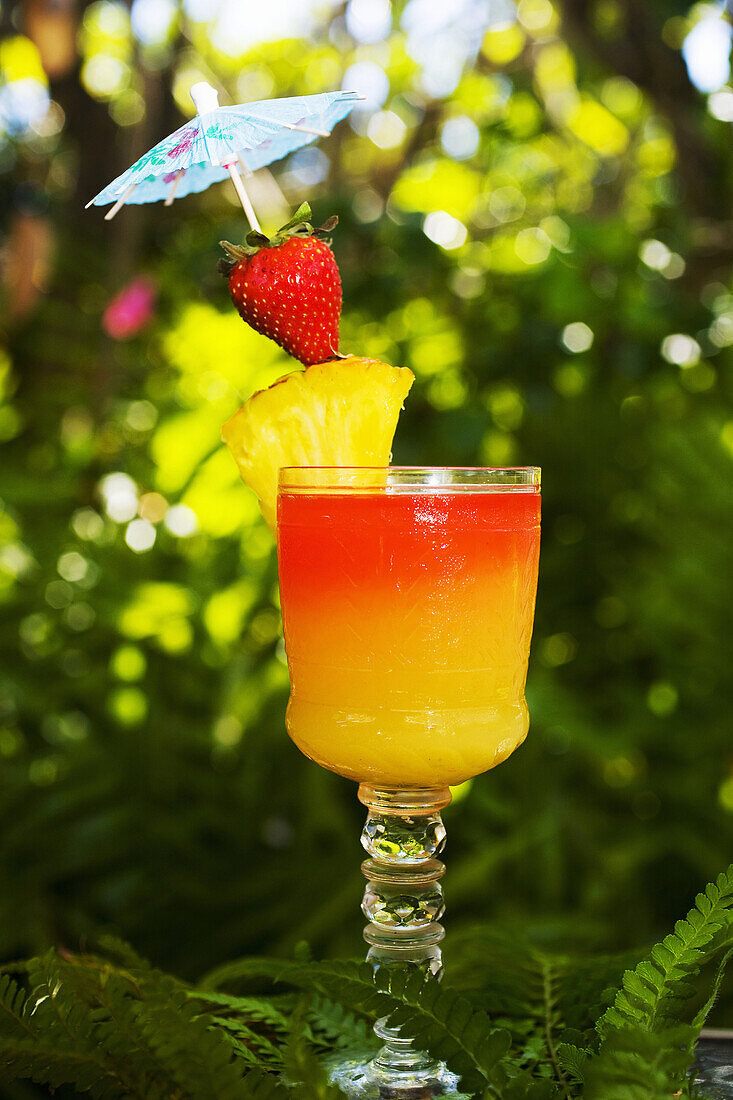 A Tequila Sunrise Garnished With Fruit In An Outdoor Setting.
