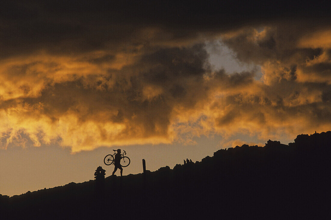 Mountain Biker Carries Bike Up Rocky Slope, Sunset Clouds Behind, Whistler, Bc Canada